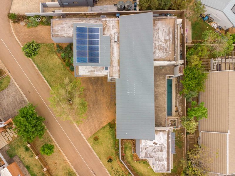 Aerial view of the property showcasing the roof structure with solar panels, paved driveway, swimming pool, and surrounding garden area.