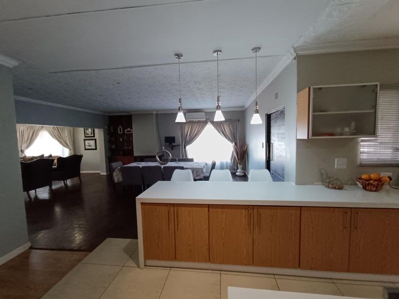 Open plan living and dining area featuring a kitchen island with cabinetry, pendant lighting, and a mix of tiled and laminate flooring.