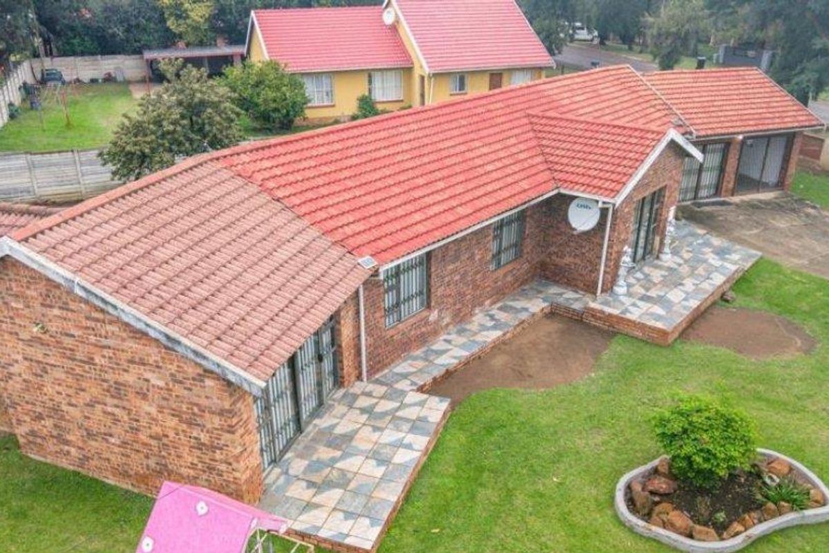 Aerial view of a brick-faced house featuring a red tiled roof, paved patio areas, and a surrounding garden.