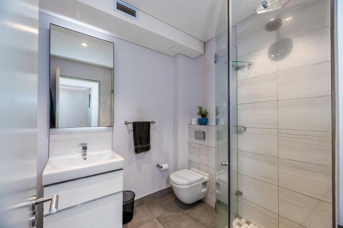 Modern bathroom featuring a wall-mounted toilet, a sleek vanity with integrated basin, and a glass-enclosed walk-in shower with tiled walls.