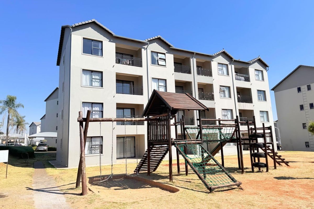 Rear view of a multi-story apartment complex featuring private balconies and a communal playground area set within a landscaped garden.