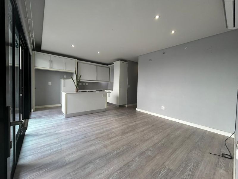 Spacious open-plan living and kitchen area featuring modern cabinetry, a central island, laminate flooring, and large sliding doors leading to an outdoor space.