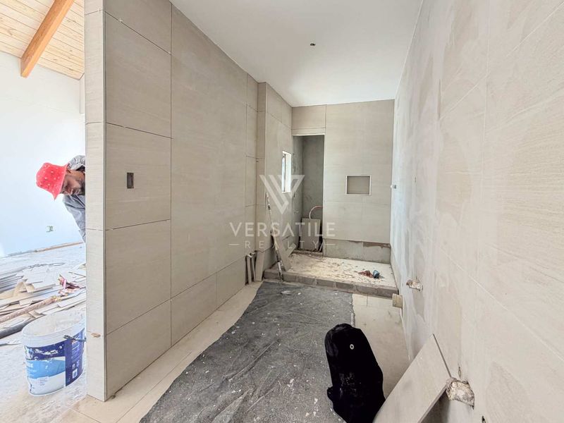 A bathroom under construction featuring large format wall tiles, a recessed niche, and exposed plumbing rough-ins, currently in the finishing stages of renovation.