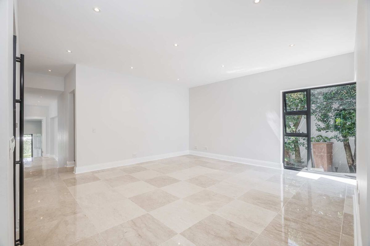 A bright and spacious living area featuring polished stone flooring, recessed downlighting, and large windows overlooking a private garden.