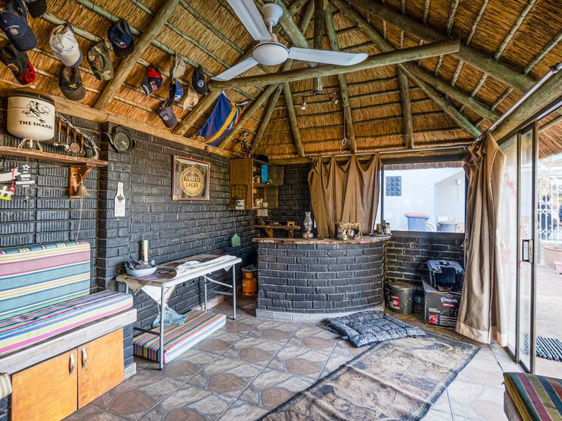 A rustic bar area featuring a thatched roof, exposed timber rafters, a built-in brick bar counter, and sliding glass doors leading to the exterior.