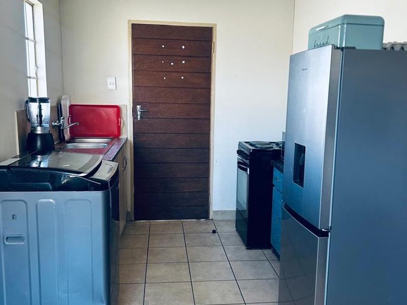 A functional kitchen area featuring tiled flooring, built-in cabinetry, and a sink, providing a practical space for meal preparation and laundry tasks.