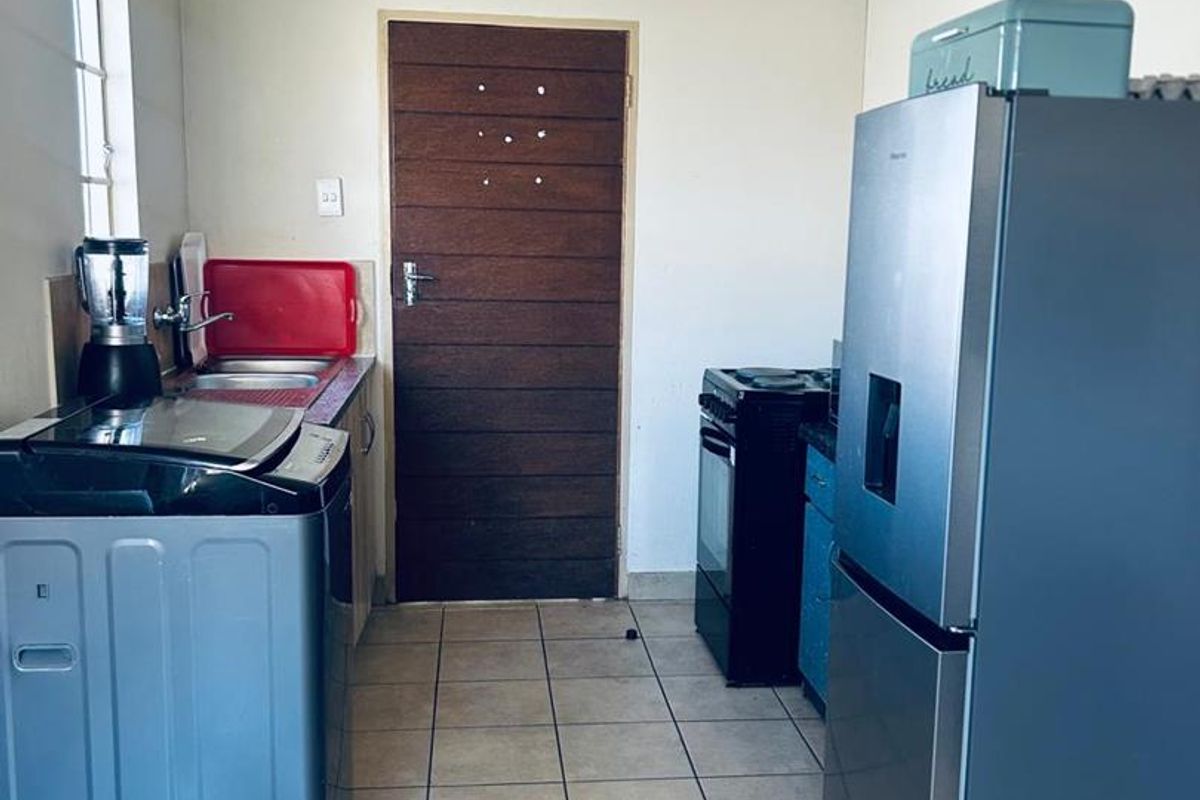 A functional kitchen area featuring tiled flooring, built-in cabinetry, and a sink, providing a practical space for meal preparation and laundry tasks.