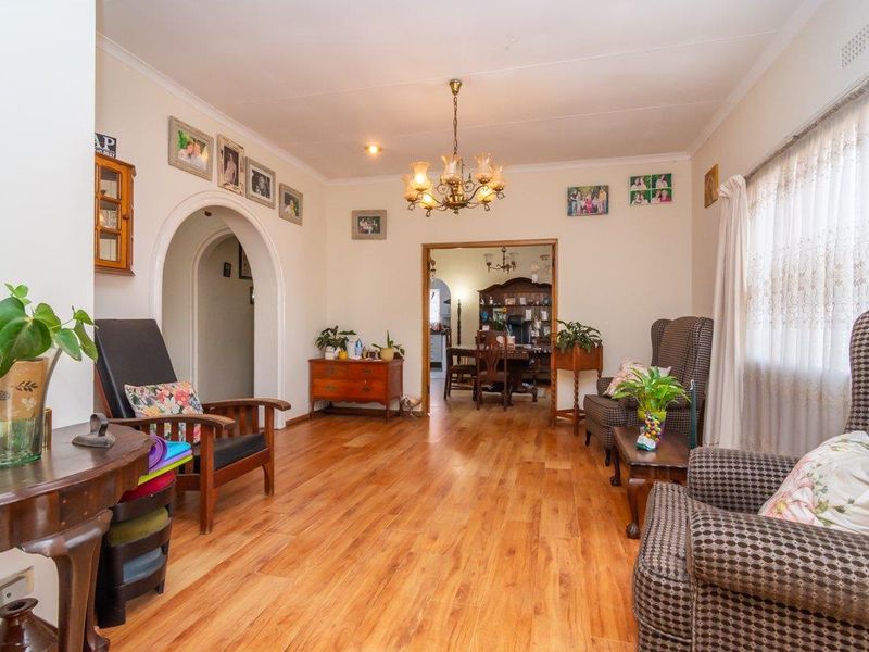 A spacious living room featuring warm laminate flooring, an elegant arched doorway, and a classic chandelier, offering a comfortable and inviting atmosphere.