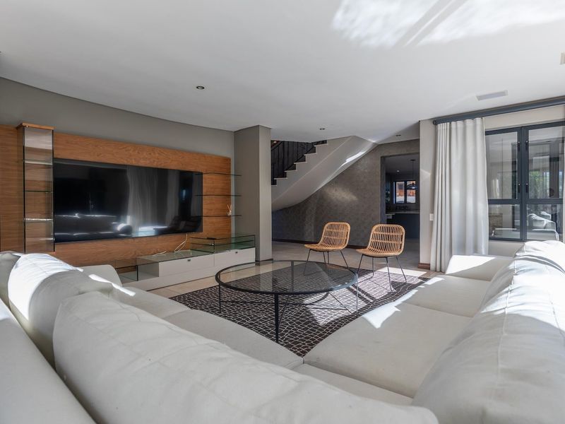 Spacious modern living room featuring a custom built-in media wall, recessed lighting, and large windows with neutral finishes throughout.