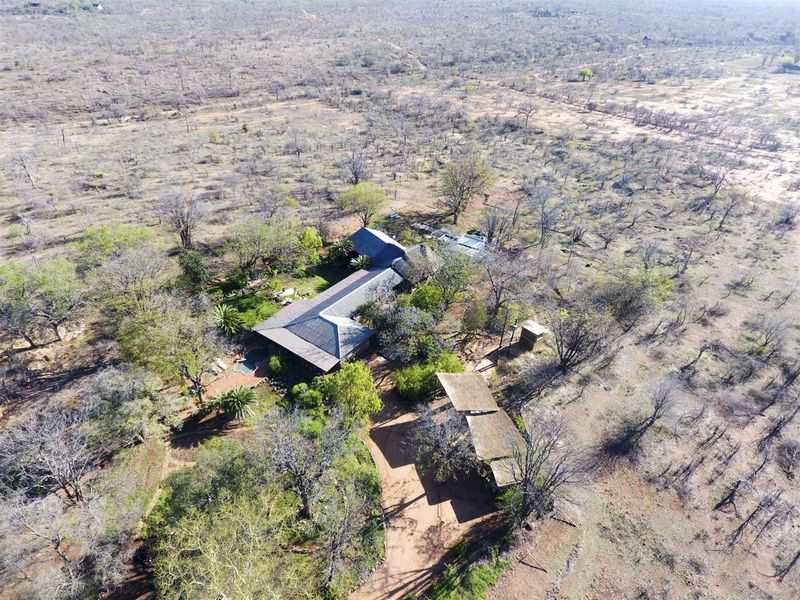 Aerial view of a property featuring a main residence with a thatched roof, a swimming pool, and an outbuilding set in a natural landscape.