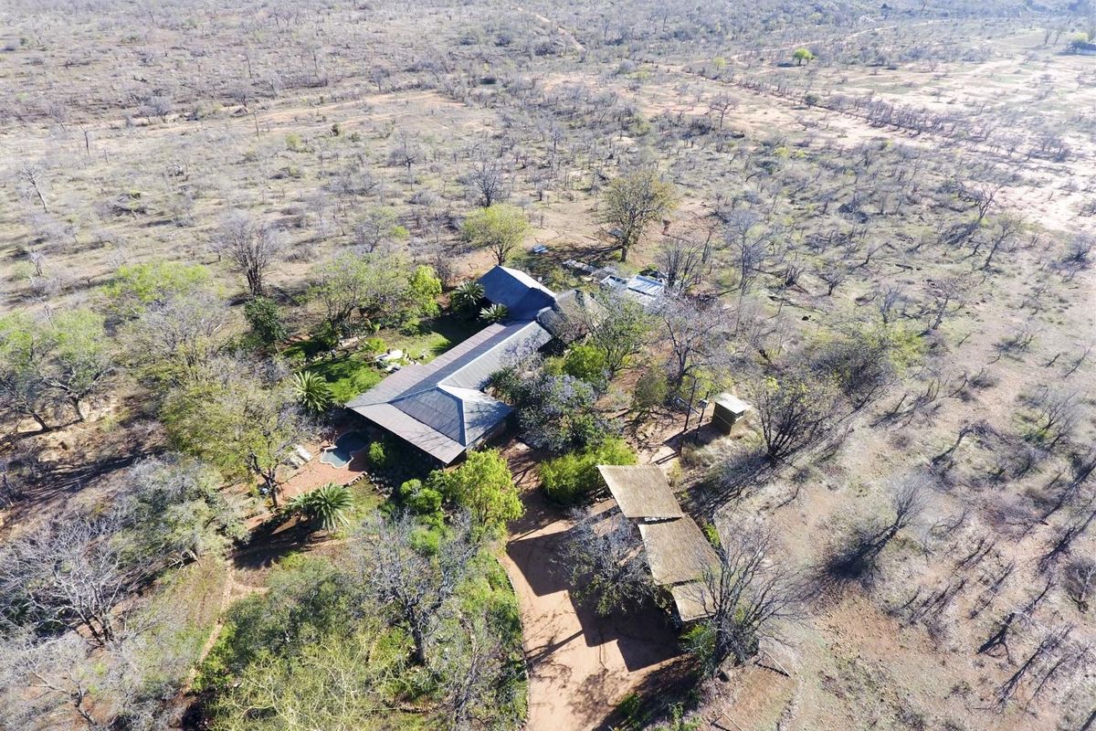 Aerial view of a property featuring a main residence with a thatched roof, a swimming pool, and an outbuilding set in a natural landscape.