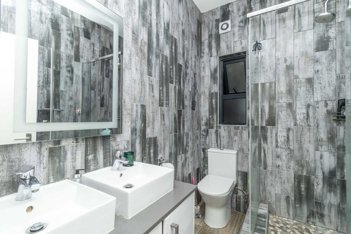 Modern bathroom featuring dual vessel sinks, a glass-enclosed shower with pebble flooring, and contemporary grey wood-look wall tiling.