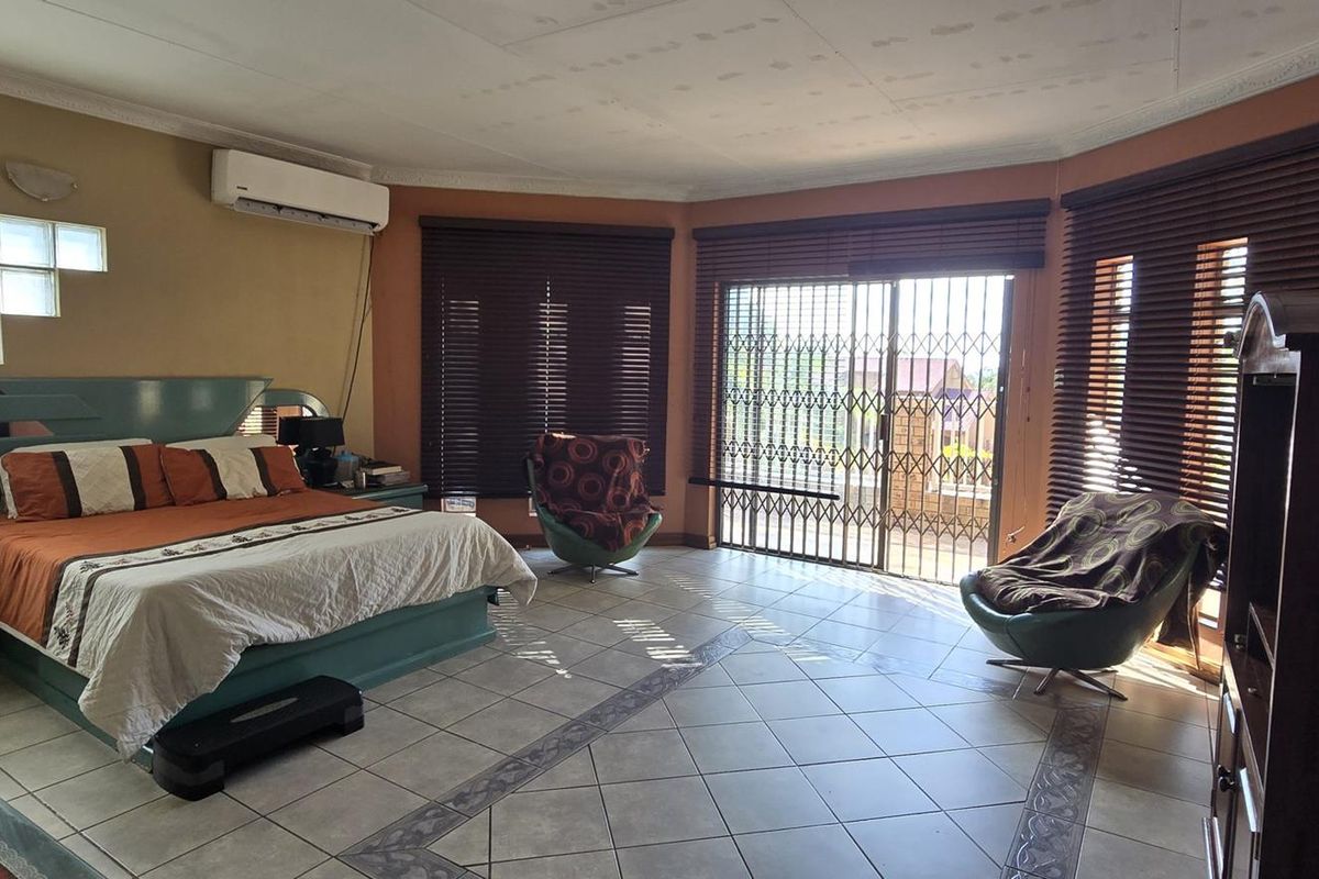Spacious bedroom featuring tiled flooring, glass block feature wall, split-system air conditioning, and sliding door access to an outdoor area with security gate.