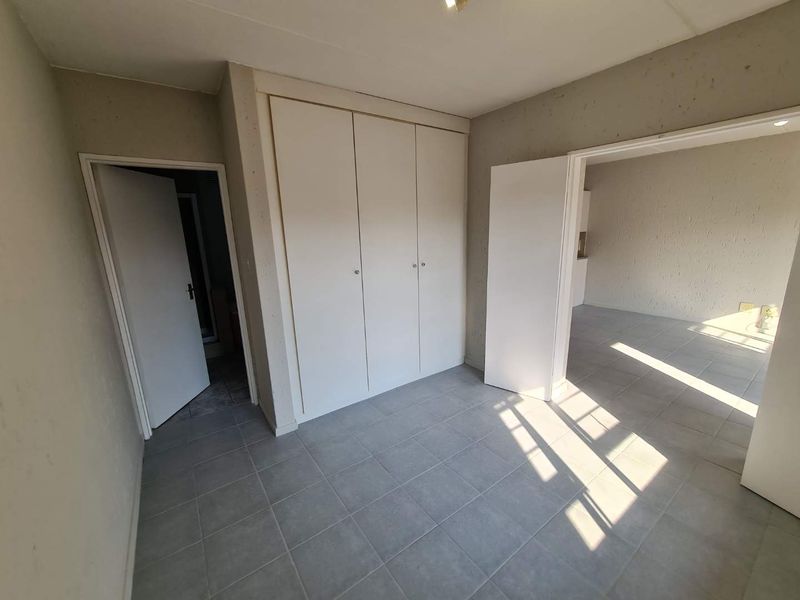 An empty bedroom featuring tiled flooring and built-in cupboards, with direct access to an adjacent room and a secondary doorway.