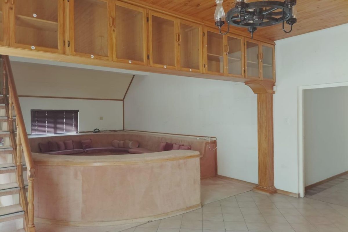 Spacious living area featuring a sunken conversation pit, built-in wooden overhead cabinetry, tiled flooring, and a timber-clad ceiling with a decorative chandelier.