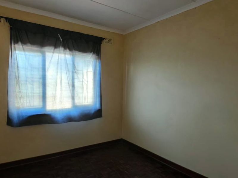 An empty bedroom featuring parquet flooring, security bars on the window, and neutral wall finishes, offering a blank canvas for renovation.