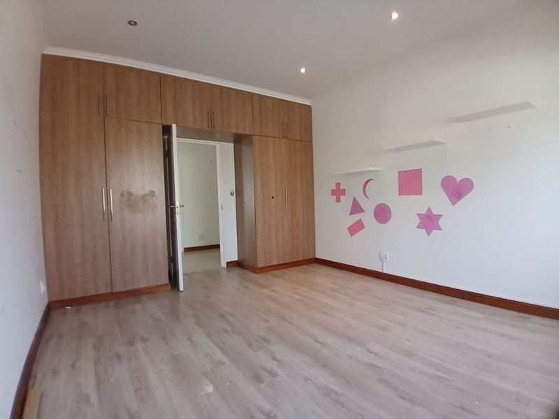 A spacious bedroom featuring light wood-look laminate flooring, extensive built-in cupboards, and recessed ceiling lighting, offering a clean and functional living space.