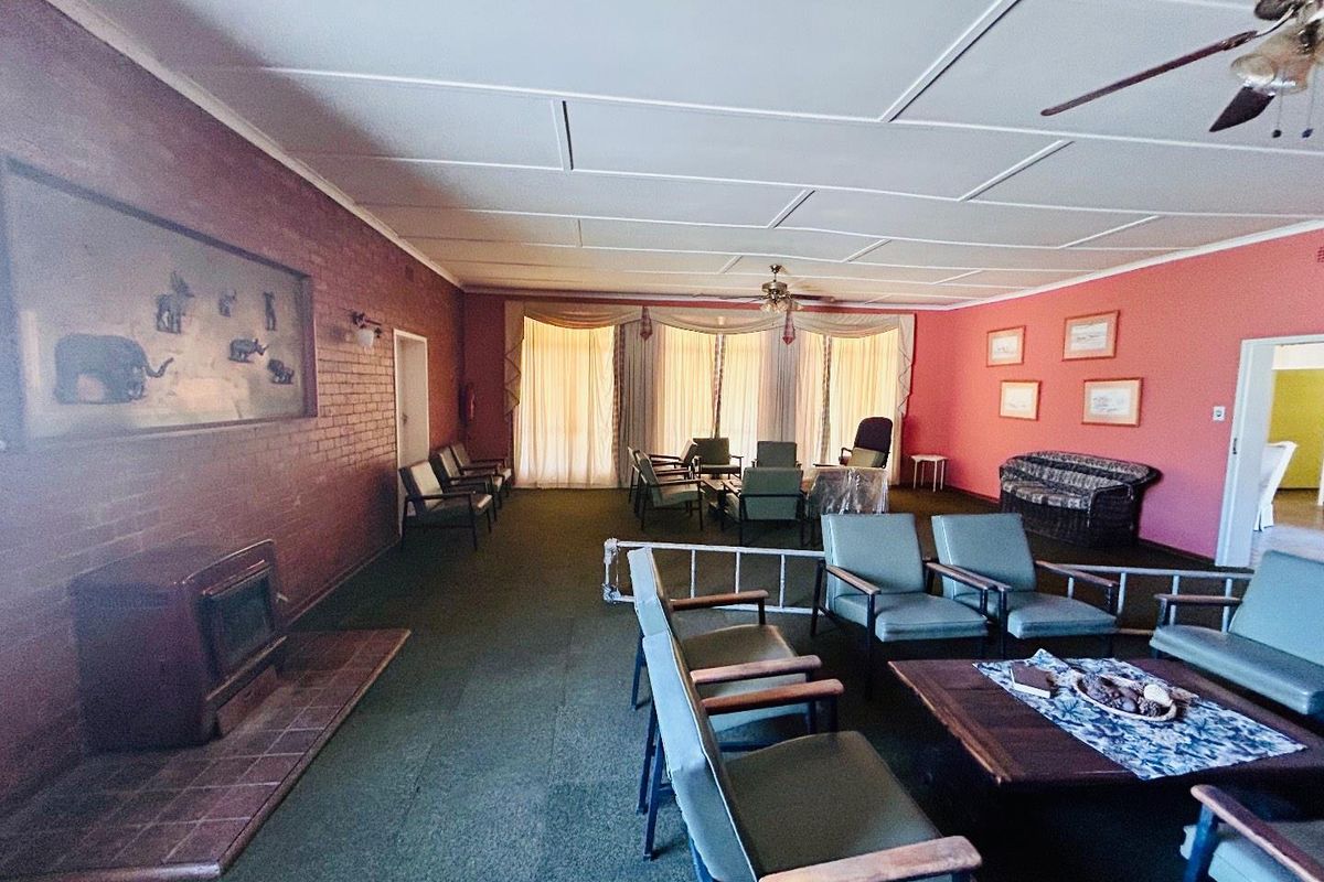 Spacious living area featuring a brick fireplace, ceiling fans, and large windows with natural light, offering a dated but functional layout.