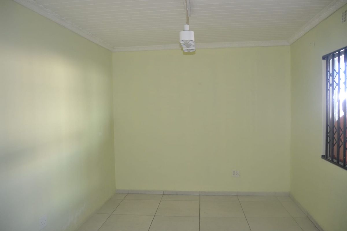 A vacant bedroom featuring tiled flooring, a security gate on the window, and a simple pendant light fixture.