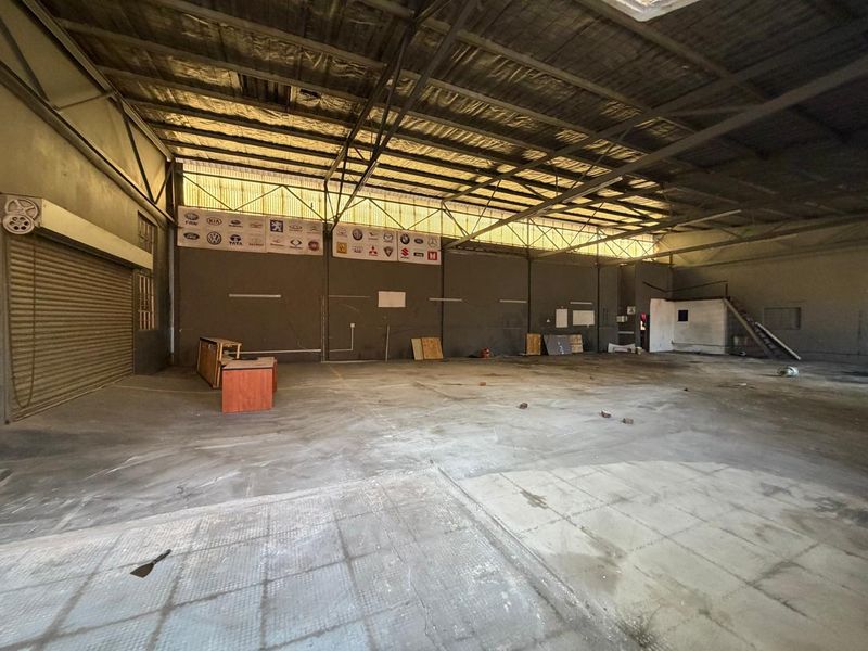 A spacious industrial utility area featuring high exposed steel roof trusses, concrete flooring, and a large roller shutter door, suitable for workshop or storage use.