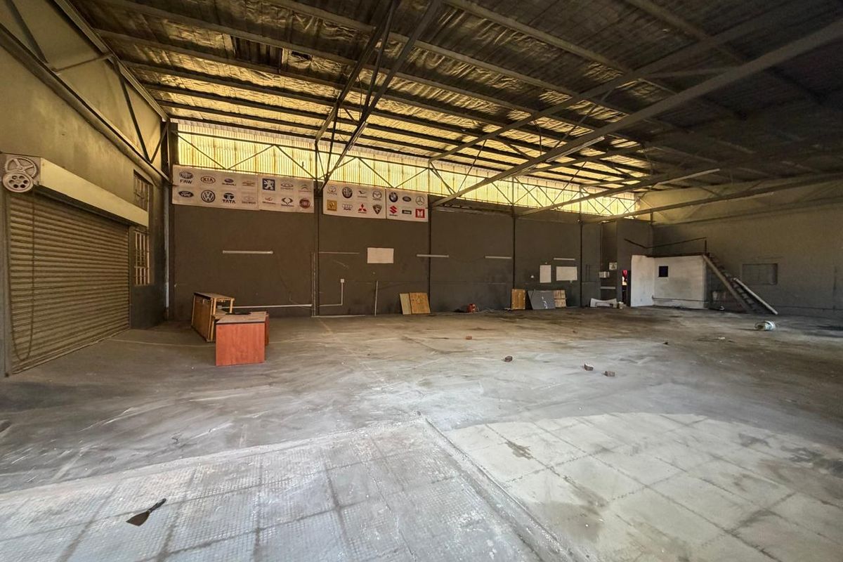 A spacious industrial utility area featuring high exposed steel roof trusses, concrete flooring, and a large roller shutter door, suitable for workshop or storage use.