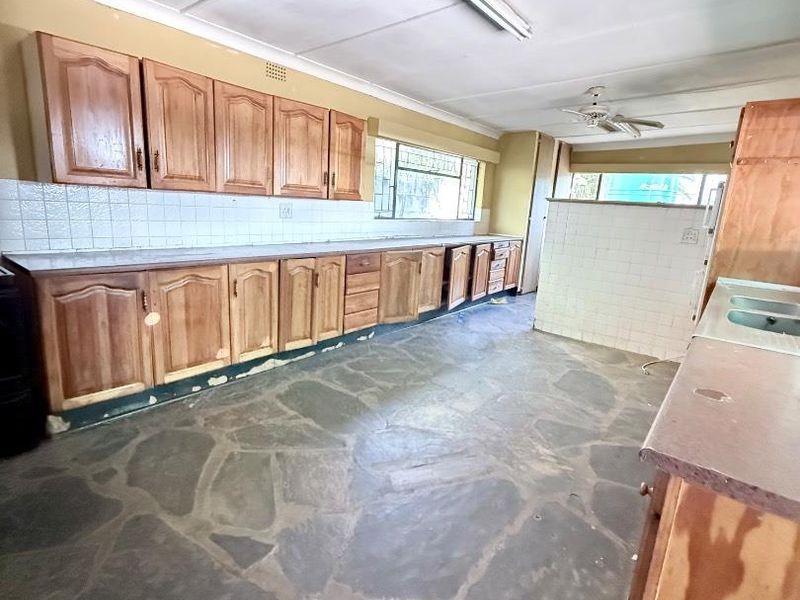 Spacious kitchen featuring traditional wooden cabinetry, stone flooring, and a tiled backsplash, offering a functional layout ready for modern renovation and updates.