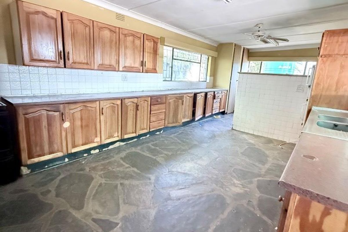 Spacious kitchen featuring traditional wooden cabinetry, stone flooring, and a tiled backsplash, offering a functional layout ready for modern renovation and updates.