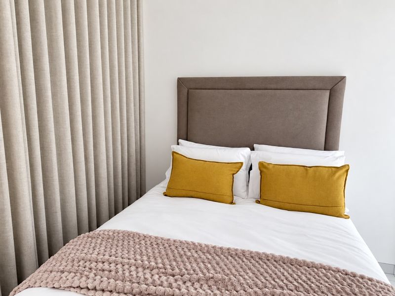 A well-maintained bedroom featuring neutral wall finishes and floor-to-ceiling curtains.