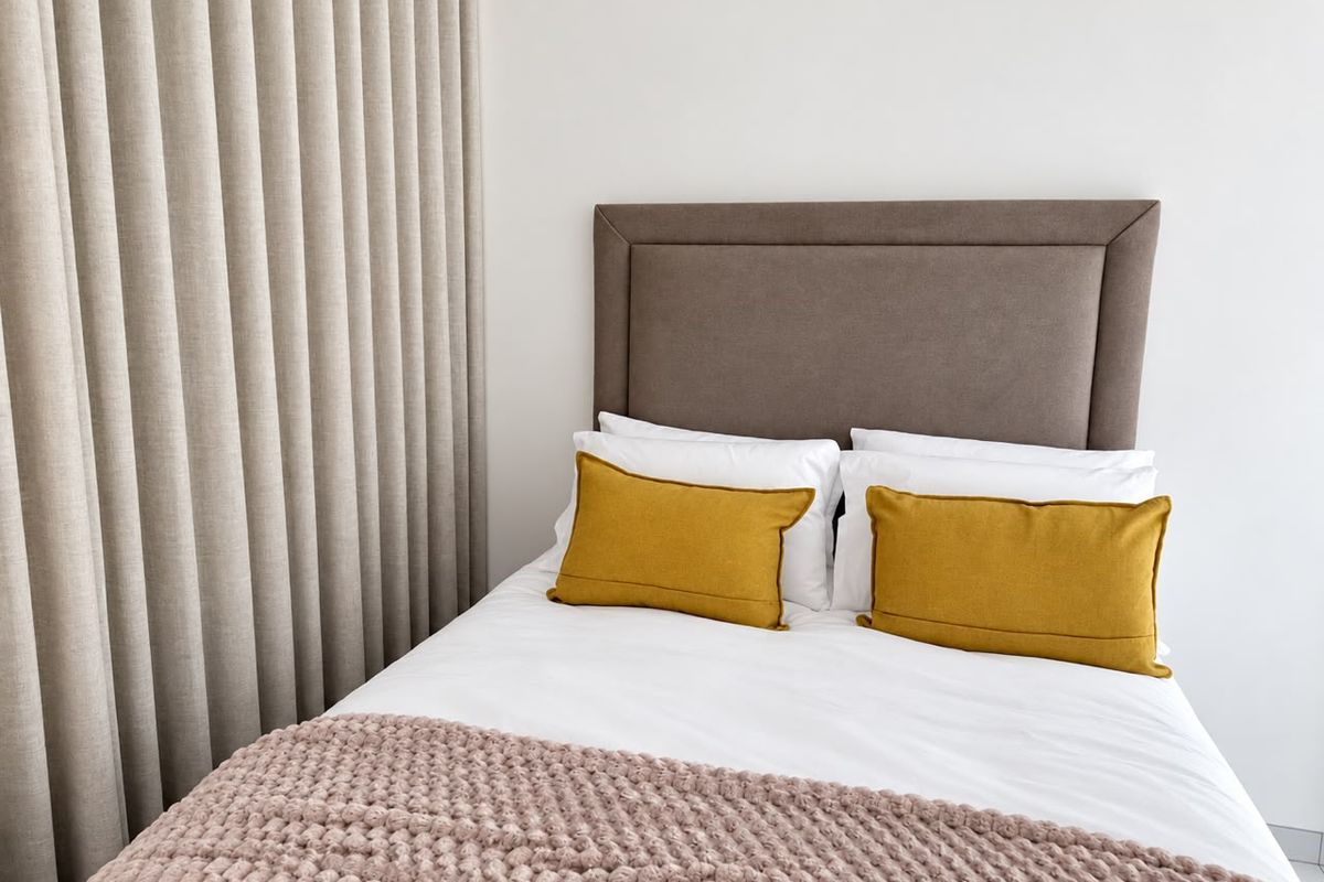 A well-maintained bedroom featuring neutral wall finishes and floor-to-ceiling curtains.