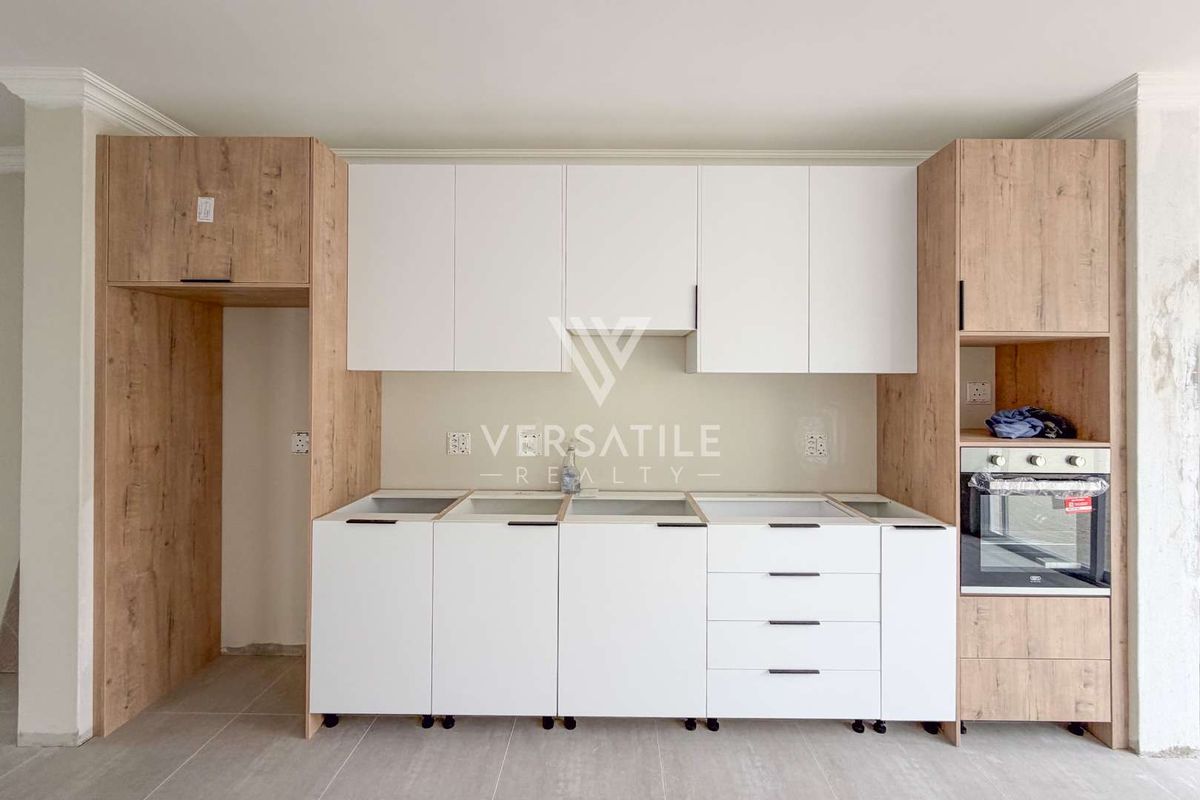 A modern kitchen area featuring two-tone cabinetry and a built-in oven, currently awaiting countertop installation and final finishing touches.