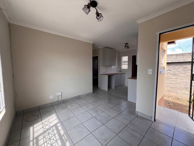 An open-plan living and kitchen area featuring neutral tiled flooring, built-in cabinetry, and direct access to an outdoor space through a security gate.