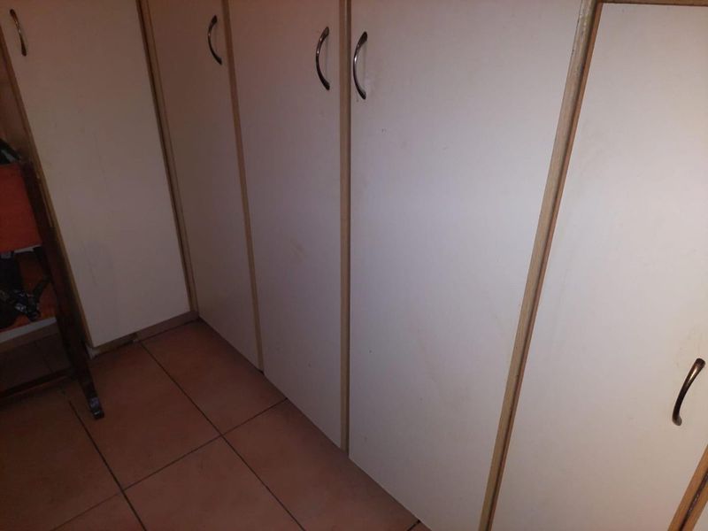 A hallway featuring built-in storage cupboards with tiled flooring, showing signs of wear and tear on the cabinetry surfaces.