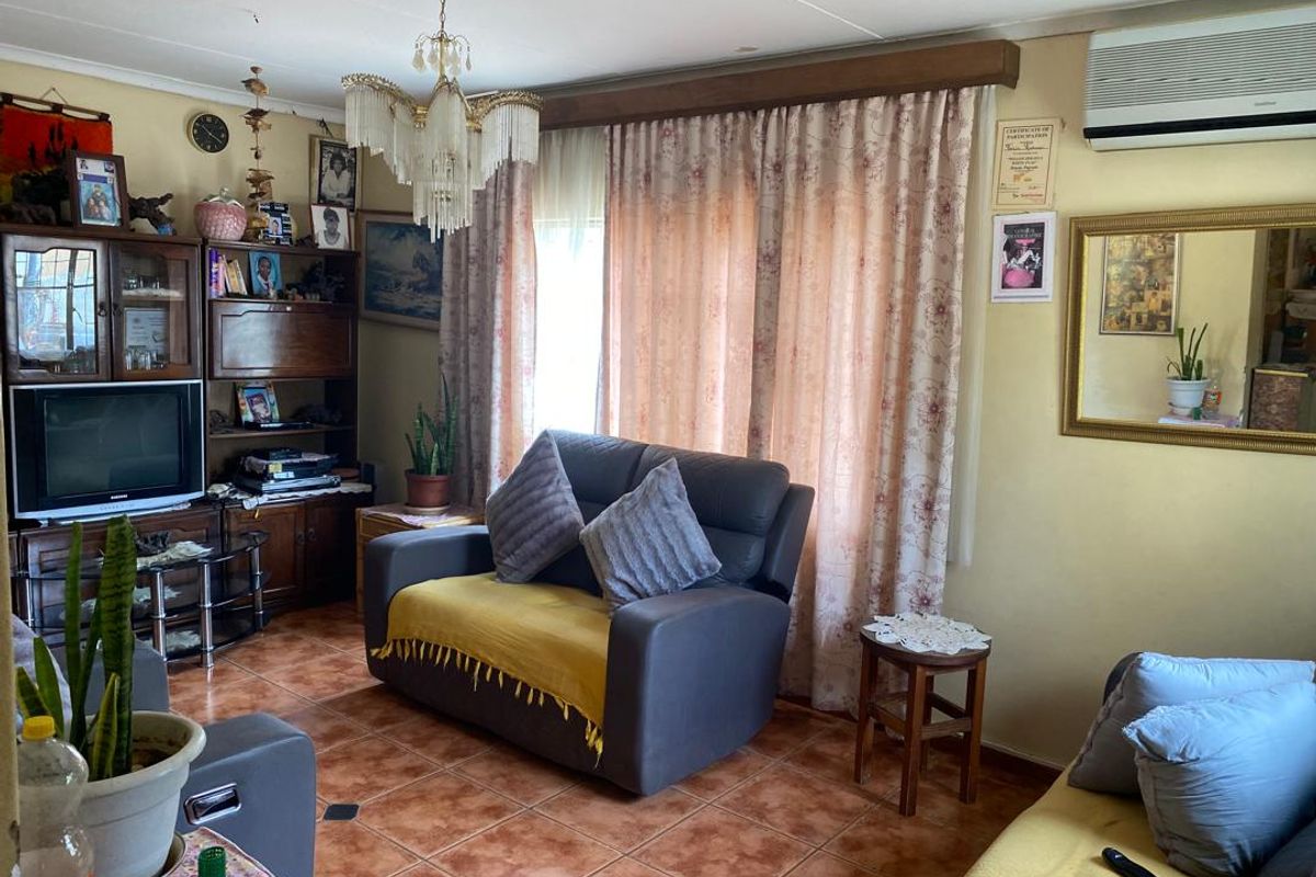 A living room featuring tiled flooring, a wall-mounted air conditioning unit, and a decorative chandelier.
