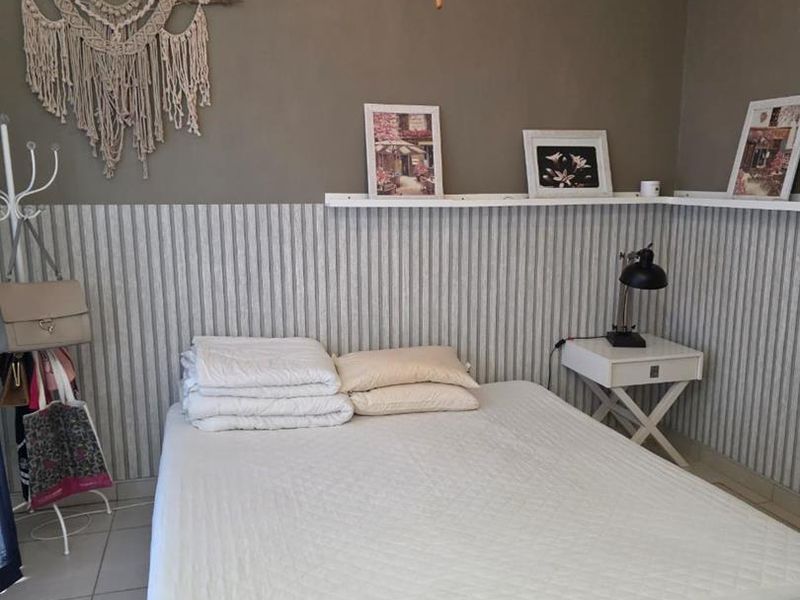 A bedroom featuring wainscoting, wall-mounted shelving, and a ceiling fan, providing a functional space with neutral wall tones.