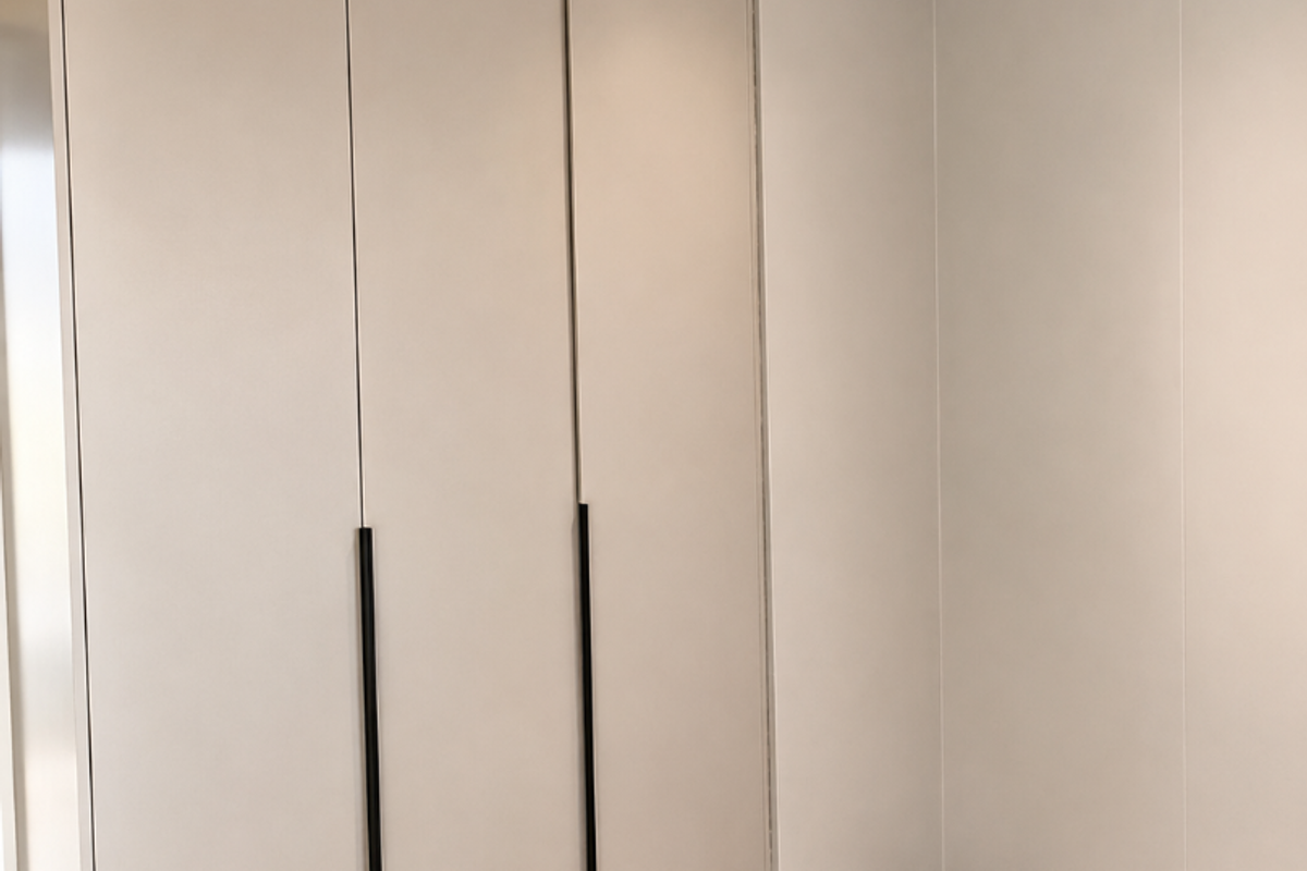 A clean, modern bedroom corner featuring neutral-toned built-in wardrobes, recessed ceiling lighting, and large format floor tiles.