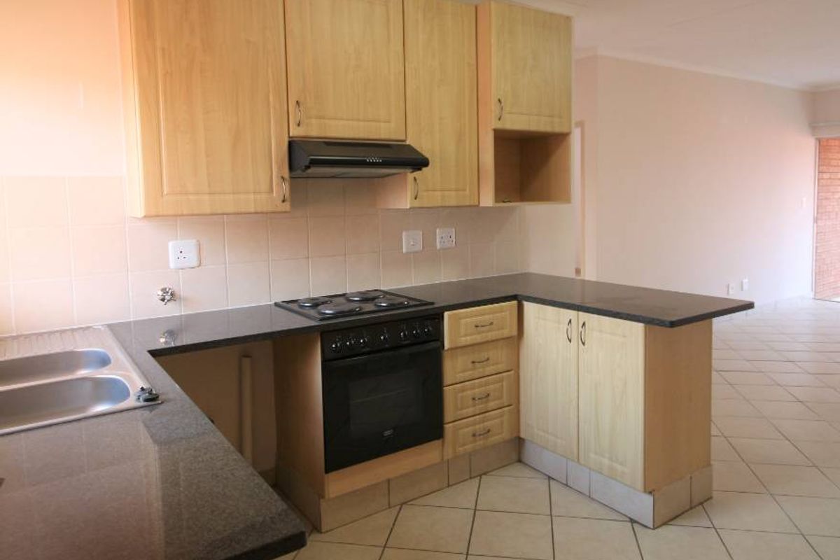 A functional kitchen featuring light wood cabinetry, granite countertops, built-in oven, hob, and extractor fan, with tiled flooring throughout.