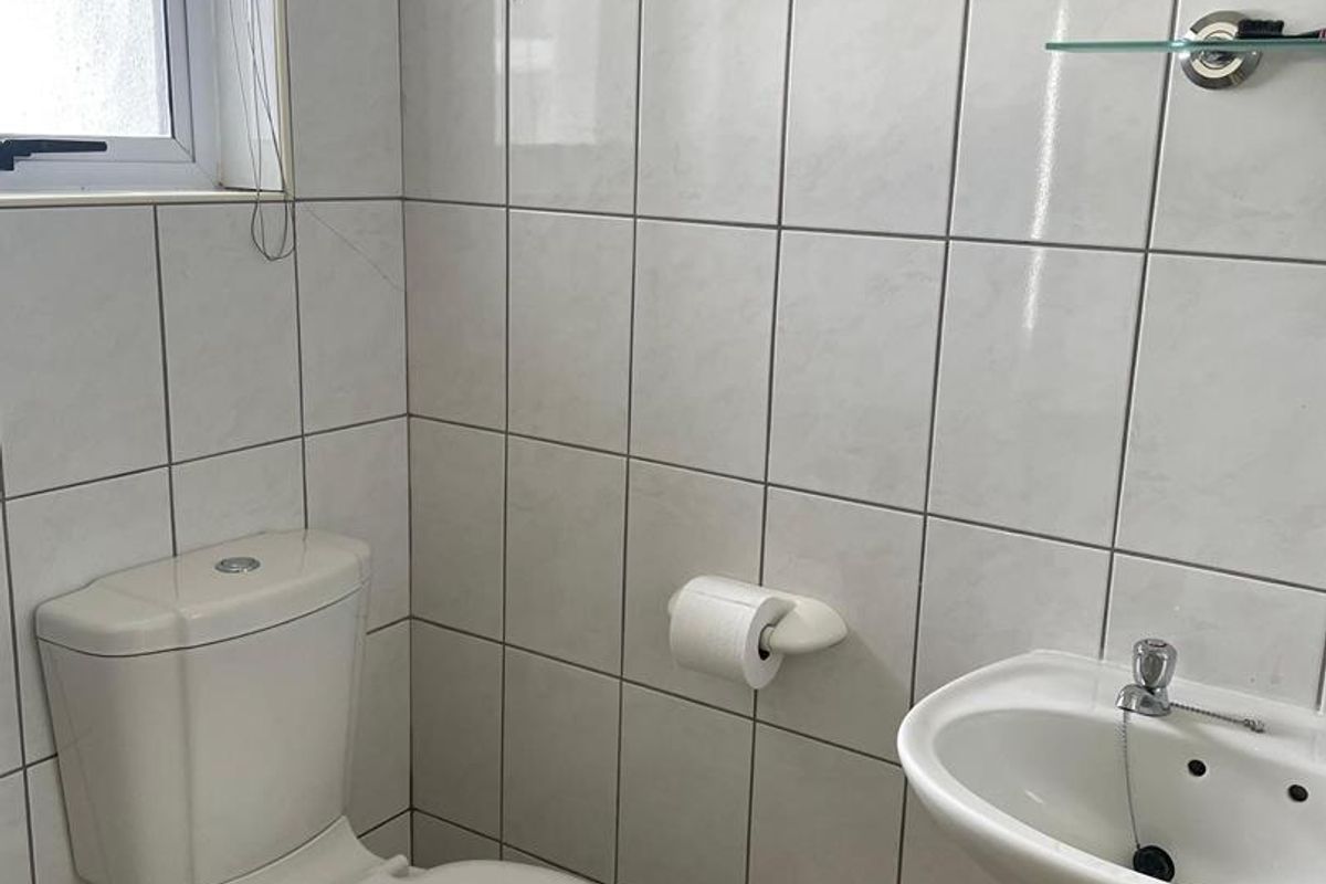 A compact bathroom featuring white wall tiles, a standard toilet, and a pedestal basin with a glass shelf.