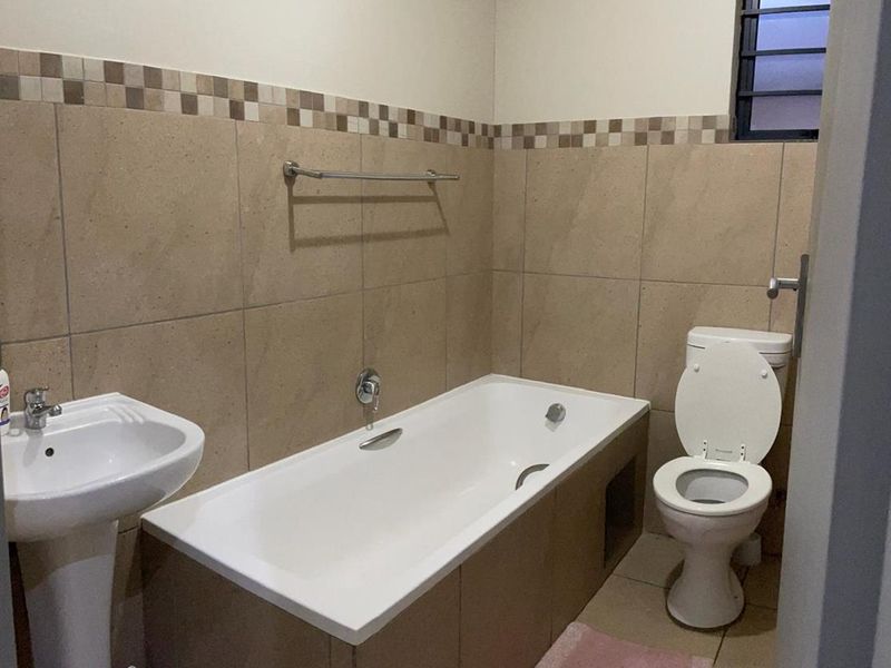 A functional bathroom featuring a pedestal basin, bathtub, and toilet with neutral wall tiling and a decorative border.