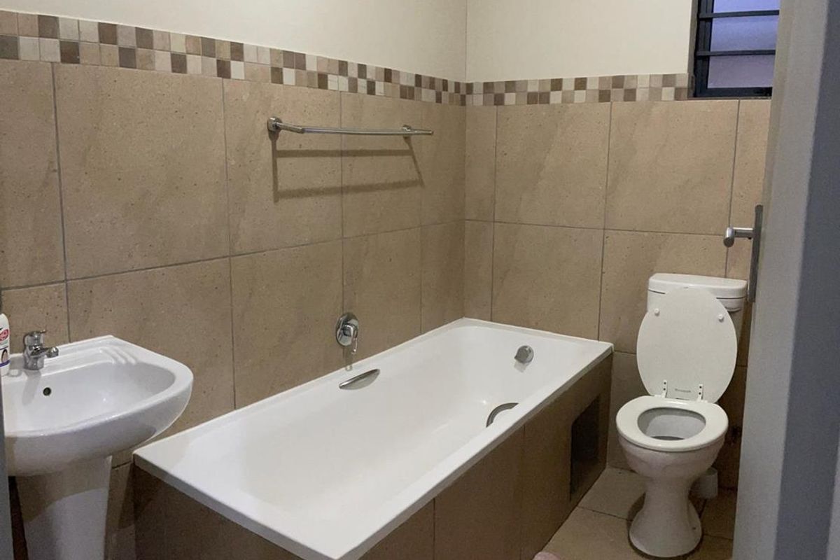 A functional bathroom featuring a pedestal basin, bathtub, and toilet with neutral wall tiling and a decorative border.