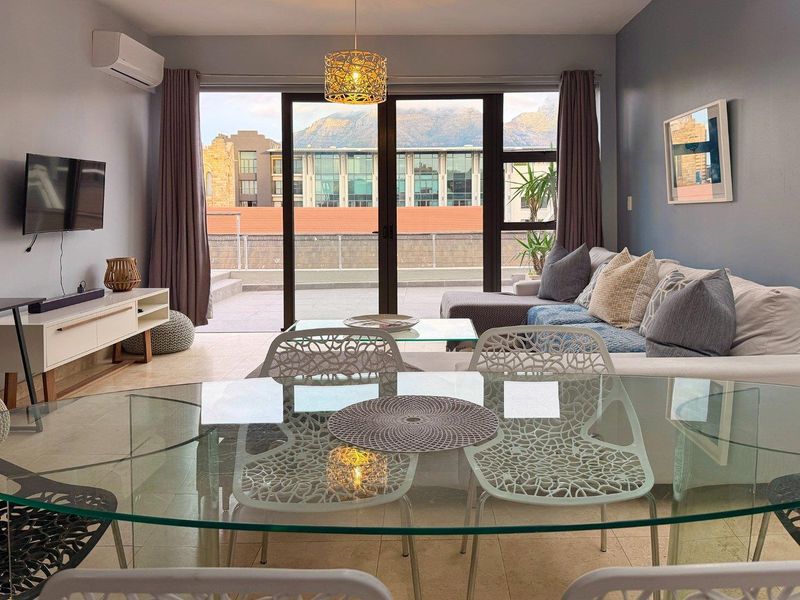 Bright open-plan living and dining area featuring tiled floors, split-system air conditioning, and large sliding glass doors opening onto a private balcony.