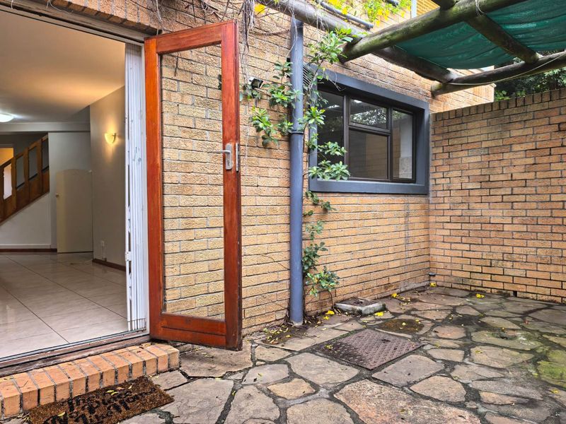 A private outdoor patio area featuring stone paving, a timber pergola, and direct access to the interior living space through a timber-framed door.