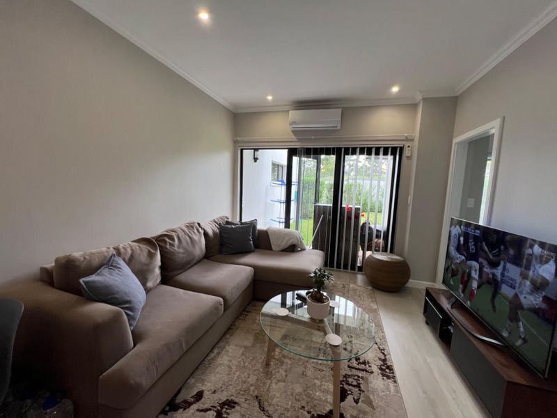 A well-maintained living room featuring laminate flooring, recessed lighting, a split-system air conditioner, and sliding glass doors leading to an outdoor area.