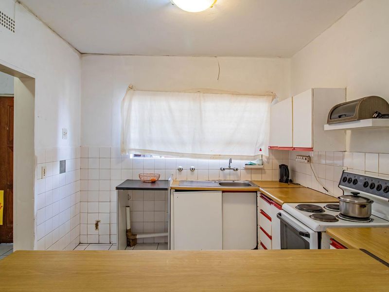 A functional kitchen featuring tiled splashbacks, laminate countertops, and a freestanding stove, offering significant potential for modernization and cosmetic updates.
