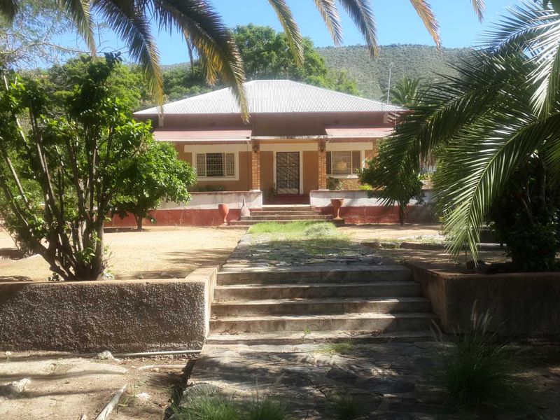 Front view of a farm-style house featuring a covered porch, stone pathway, and established garden surroundings with mountain views.