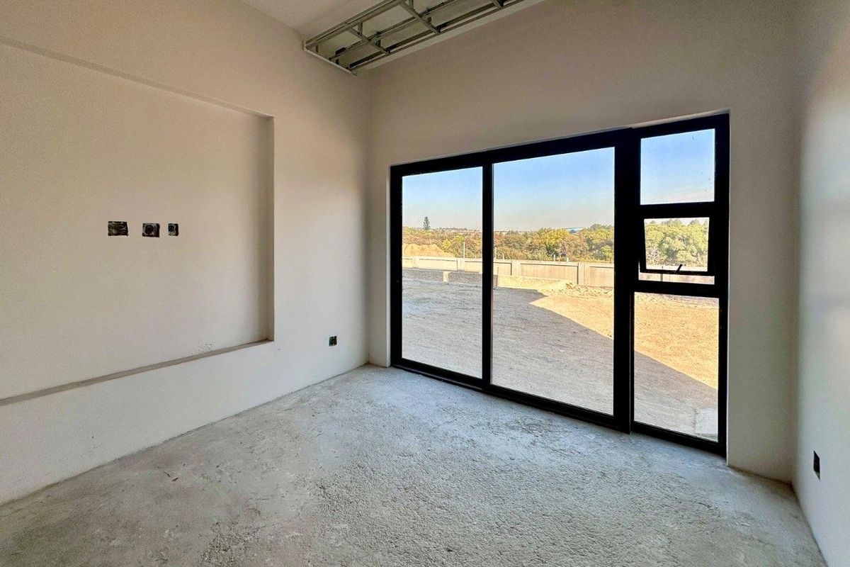 An unfinished interior space featuring large black-framed sliding glass doors, a recessed wall niche, and exposed ceiling infrastructure, ready for final flooring and ceiling installation.