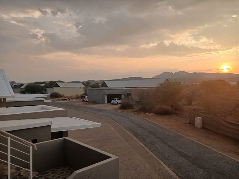 A scenic elevated view overlooking a residential estate with paved roads, modern apartment structures, and distant mountain ranges at sunset.