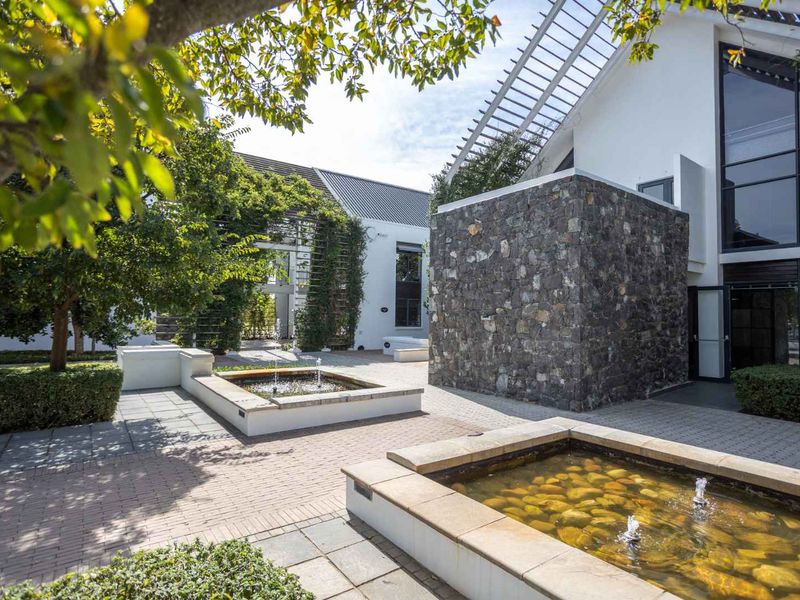 A beautifully landscaped courtyard featuring stone-clad architectural elements, tranquil water features, and paved walkways connecting modern building structures.