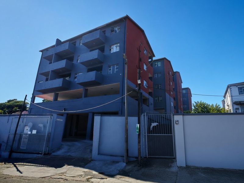 Exterior view of a multi-story apartment complex featuring balconies, secure perimeter walling, and gated driveway access.