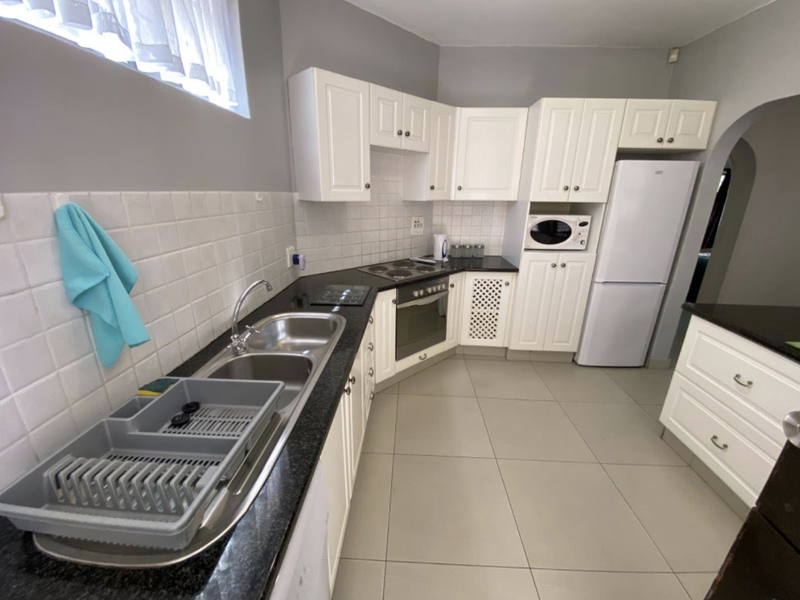 A functional kitchen featuring white cabinetry, dark granite countertops, a double basin sink, and built-in oven with electric hob.
