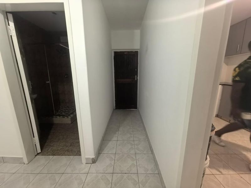 A functional hallway with tiled flooring providing access to adjacent rooms, including a bathroom and kitchen area.